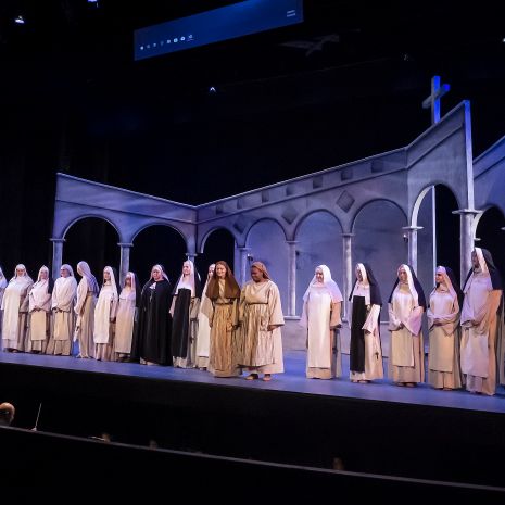 Performers lined up across stage in nun costumes, in front of set piece