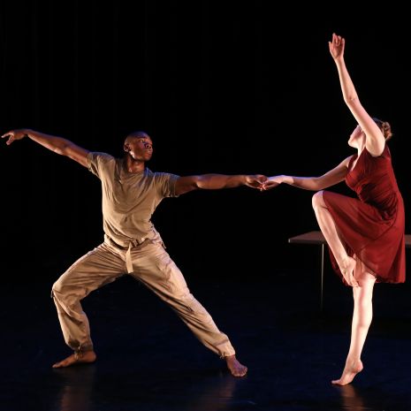Dancer in a lunge position holding the hand of another dancer one foot and arm raised