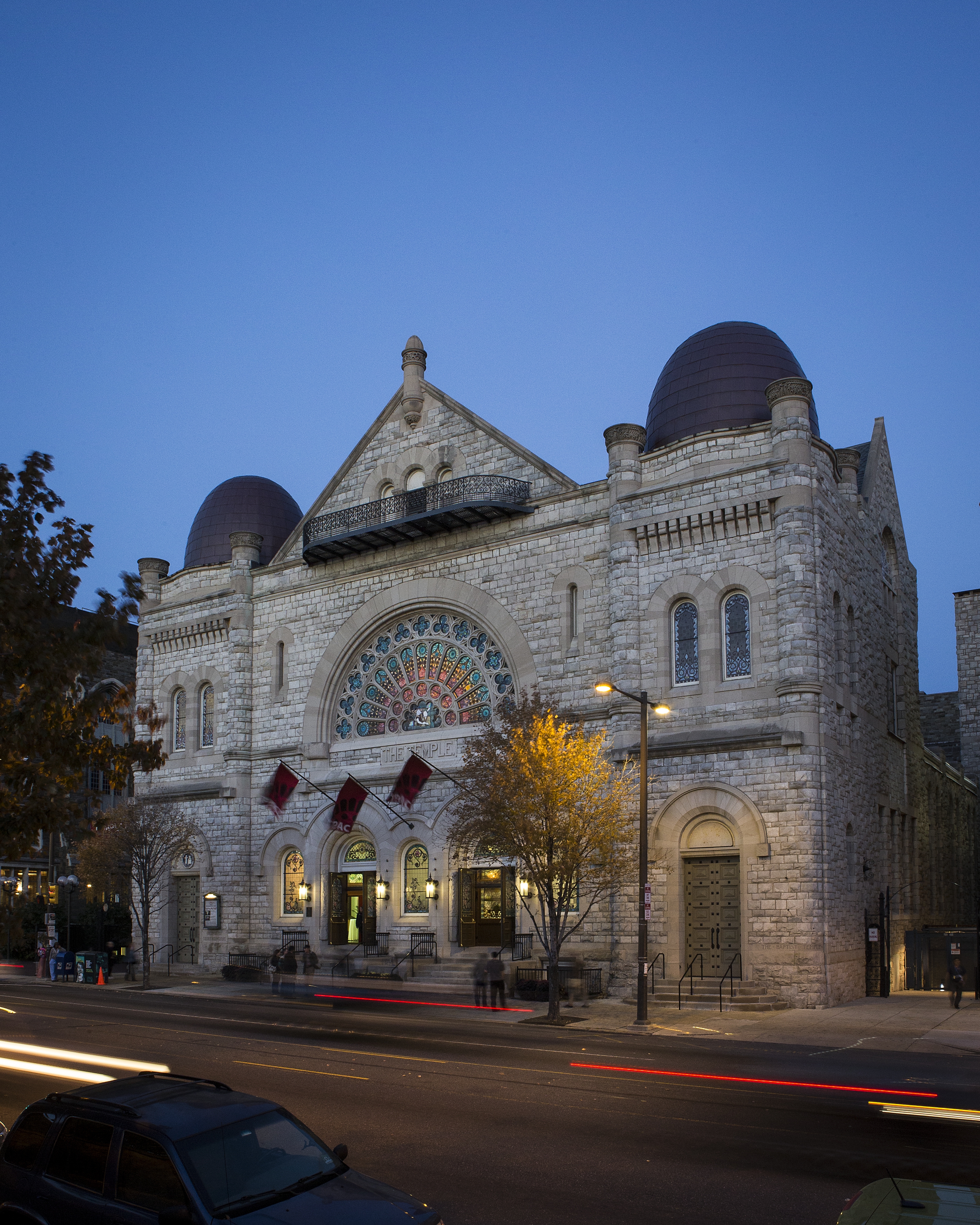 Exterior of stone church with large stained glass window, taken at night