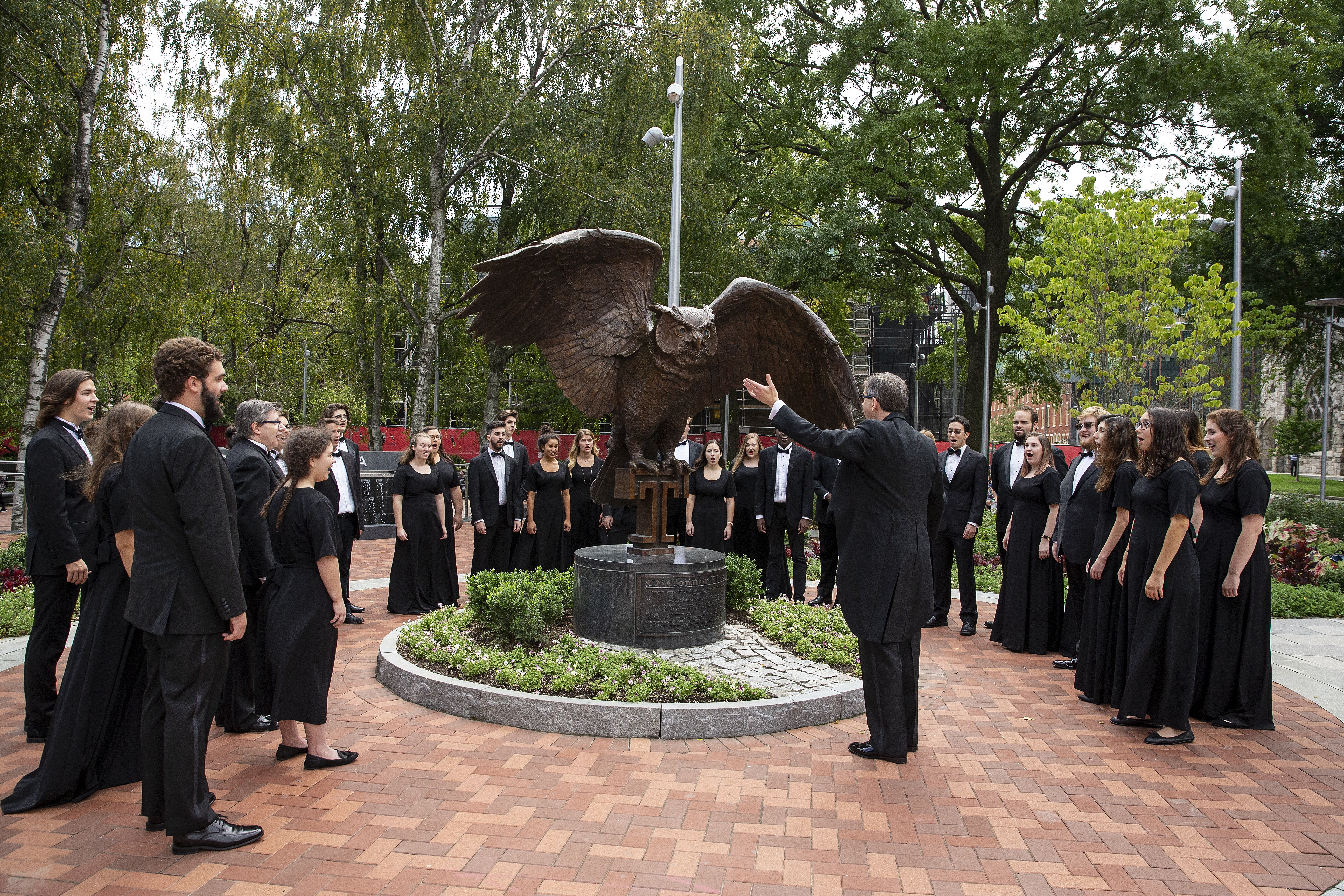 image of students dressed in concert black facing conductor in semi-circle with owl statue 