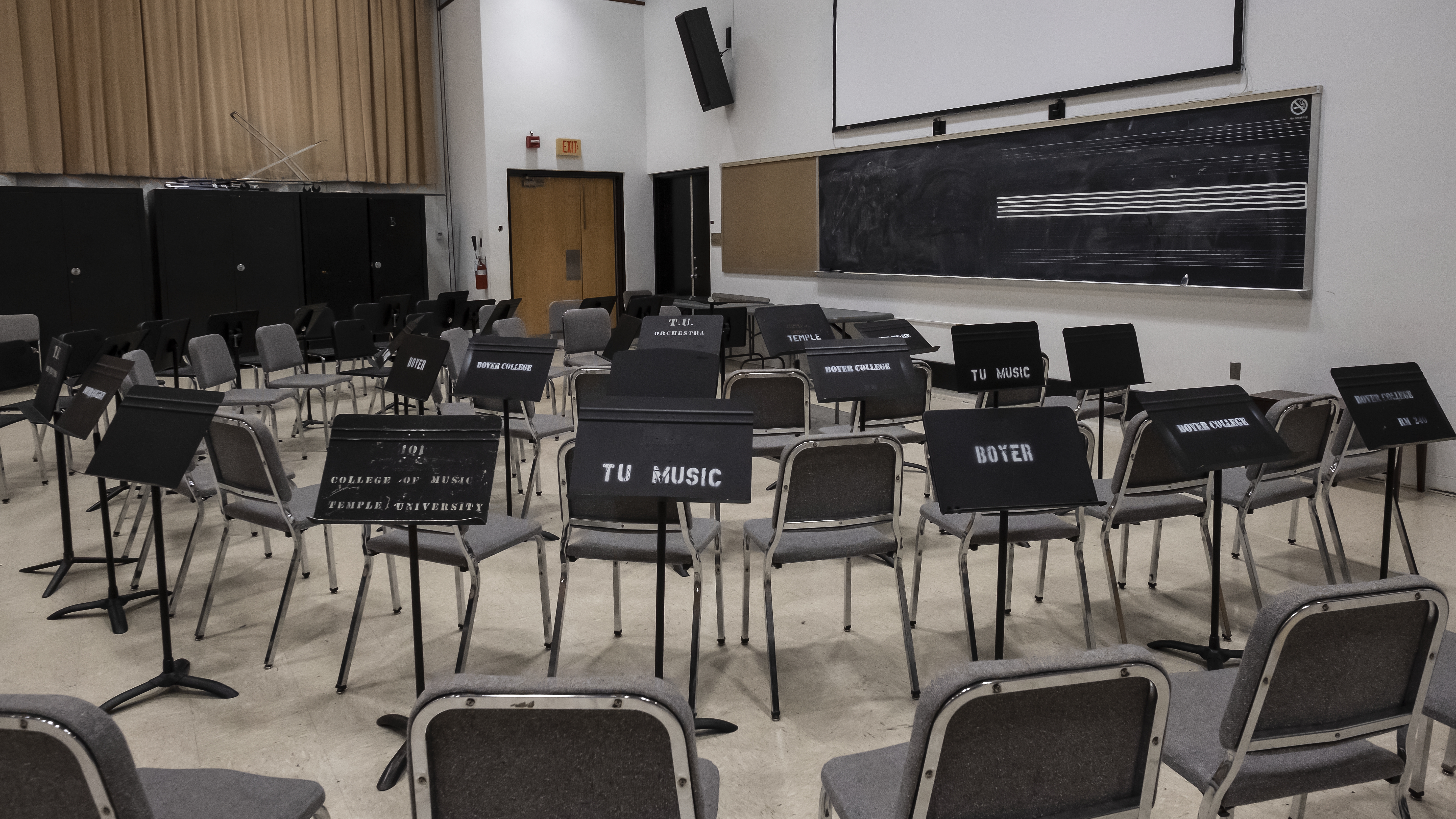Three rows of chairs in a semicircle, facing podium and chalkboard 