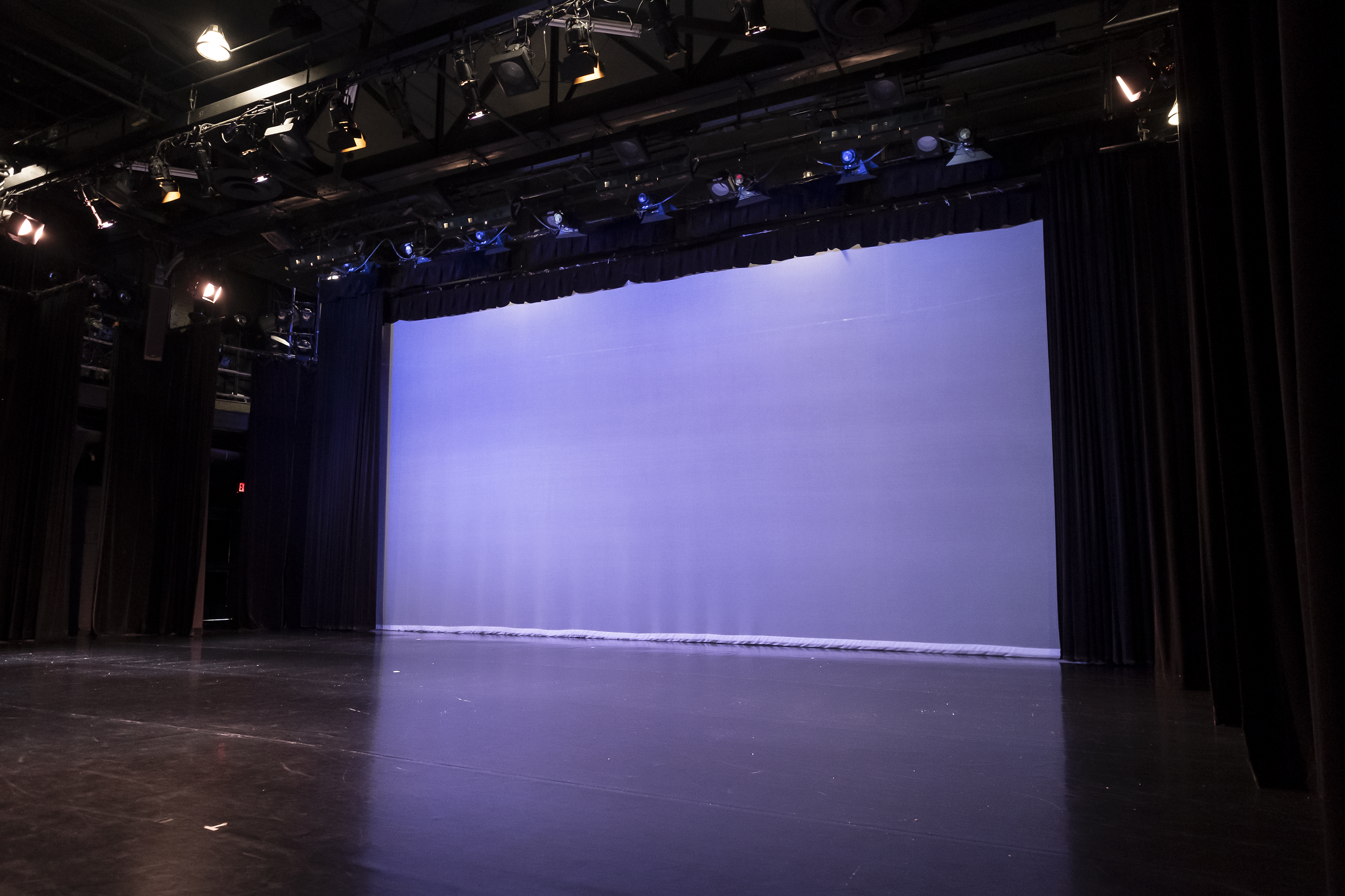 Stage in black box theater, screen in back lit with purple lights 