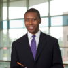 Man in a suit and purple tie smiling and holding a conducting baton