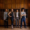 Four students stand proudly in front of a wood paneled wall.