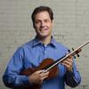 Man with dark hair and blue shirt holding a violin