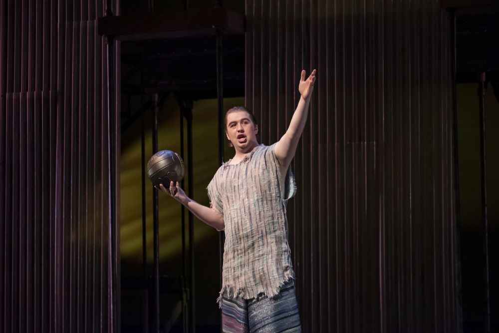 Photo of male opera student in costume and on stage with one hand holding a ball and the other stretched out