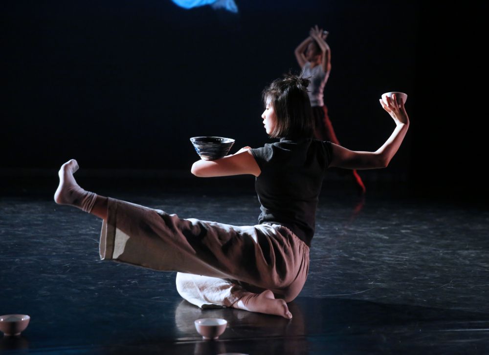 image of a dance student performing on the ground, balancing a bowl on her arm and in her hand