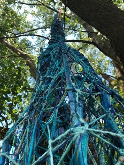 Tall blue sculpture intertwined with trees leading up into the sky