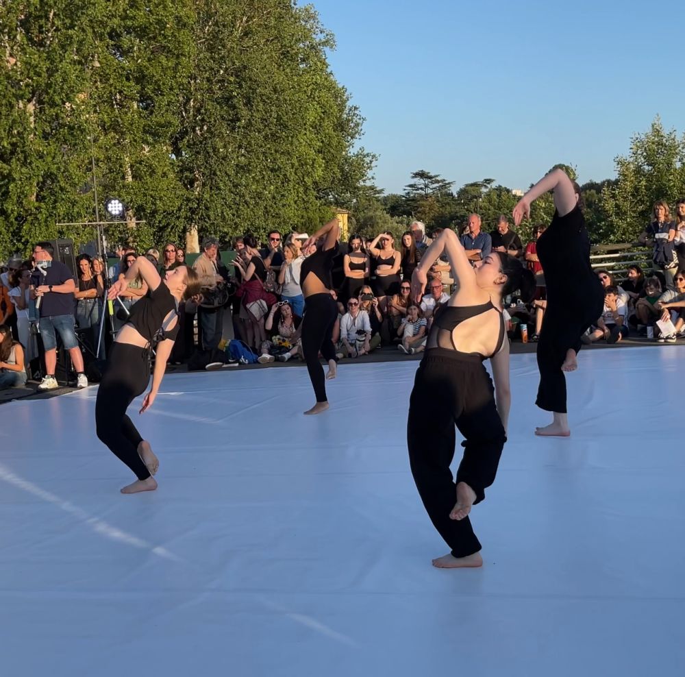 Dancers in black pants and tops perform on an outdoor stage.