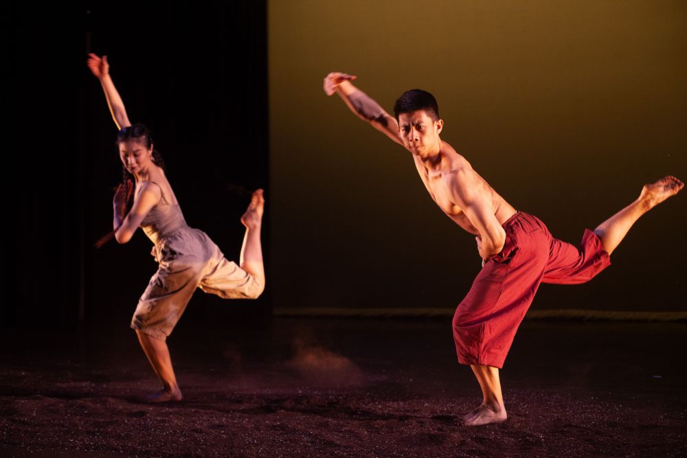 female and male dancer with arm in air and one leg behind them on stage