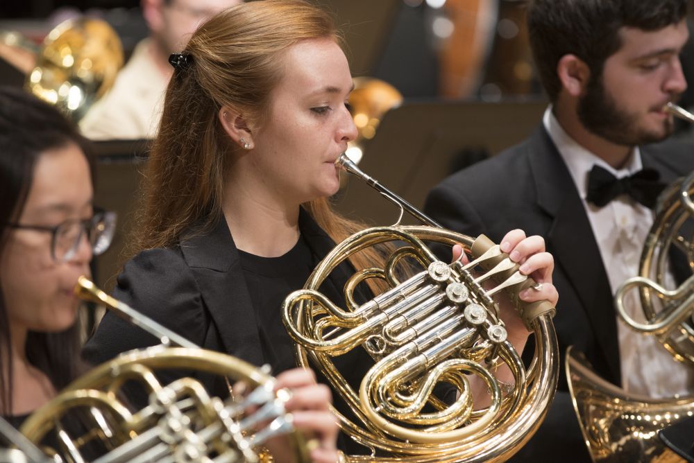 Image of three students playing french horn in an orchestra performance 