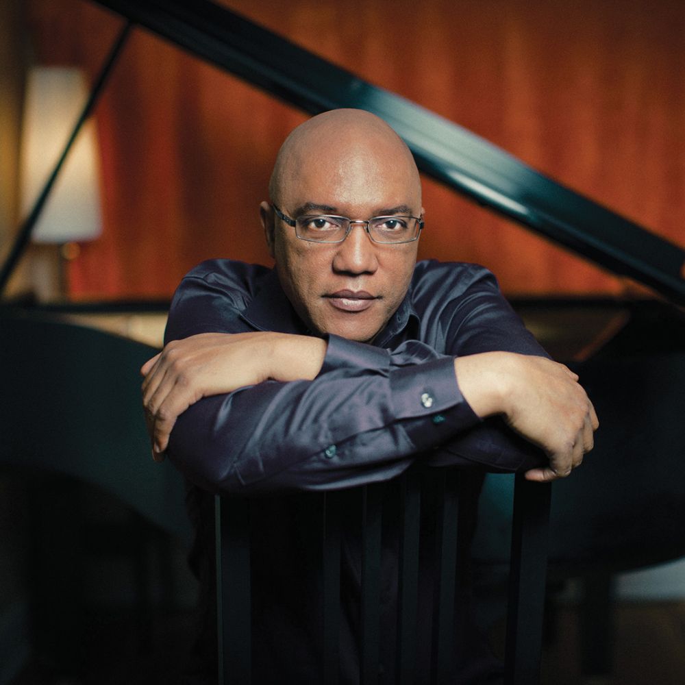 Man seated with arms crossed in front of a piano