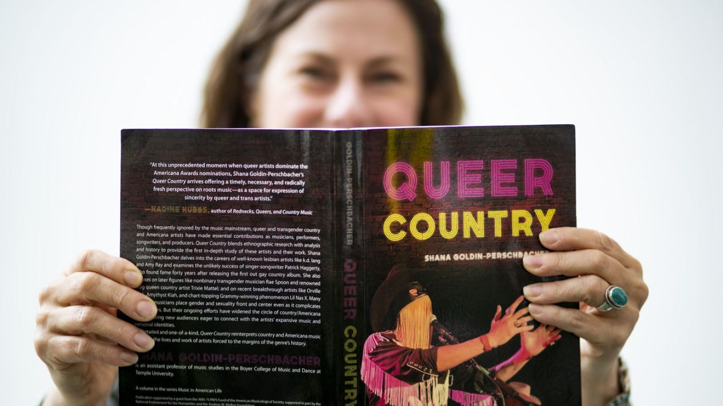 Photo of person holding Queer Country book open to show cover