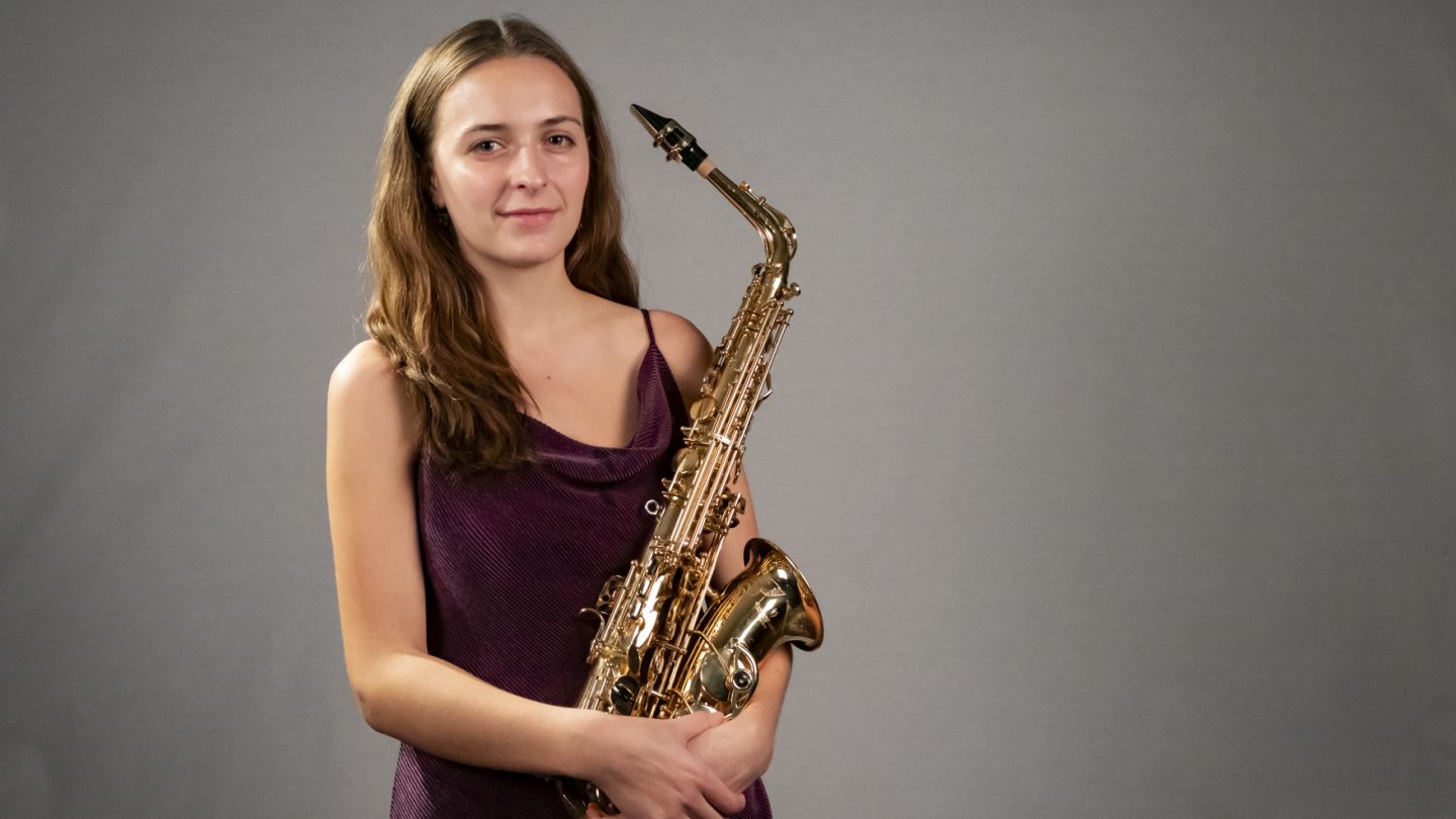 Young woman holding a saxophone against a gray backdrop