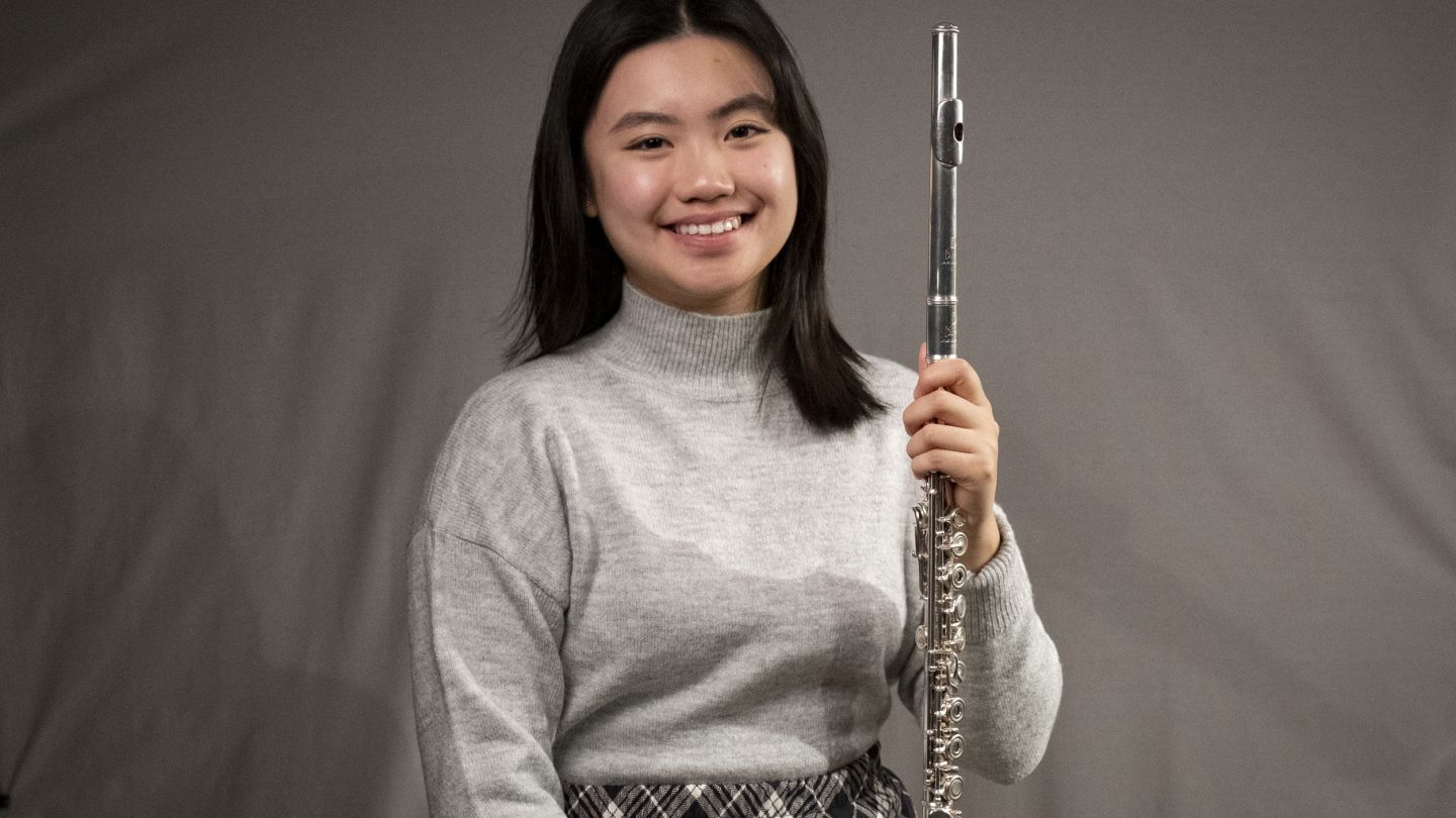 Young woman smiling and holding a flute against a gray backdrop