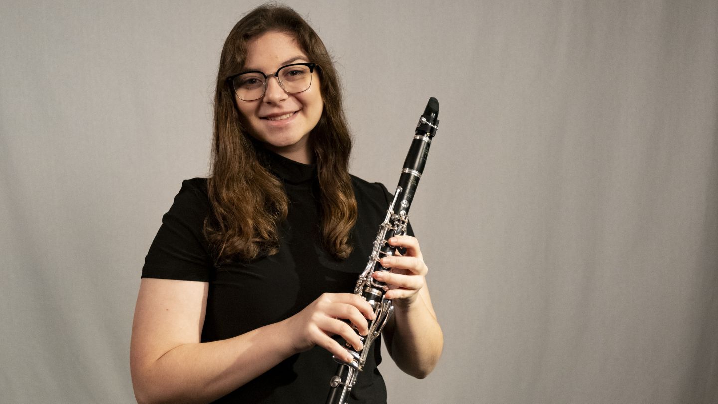 Young woman holding a clarinet against a gray background