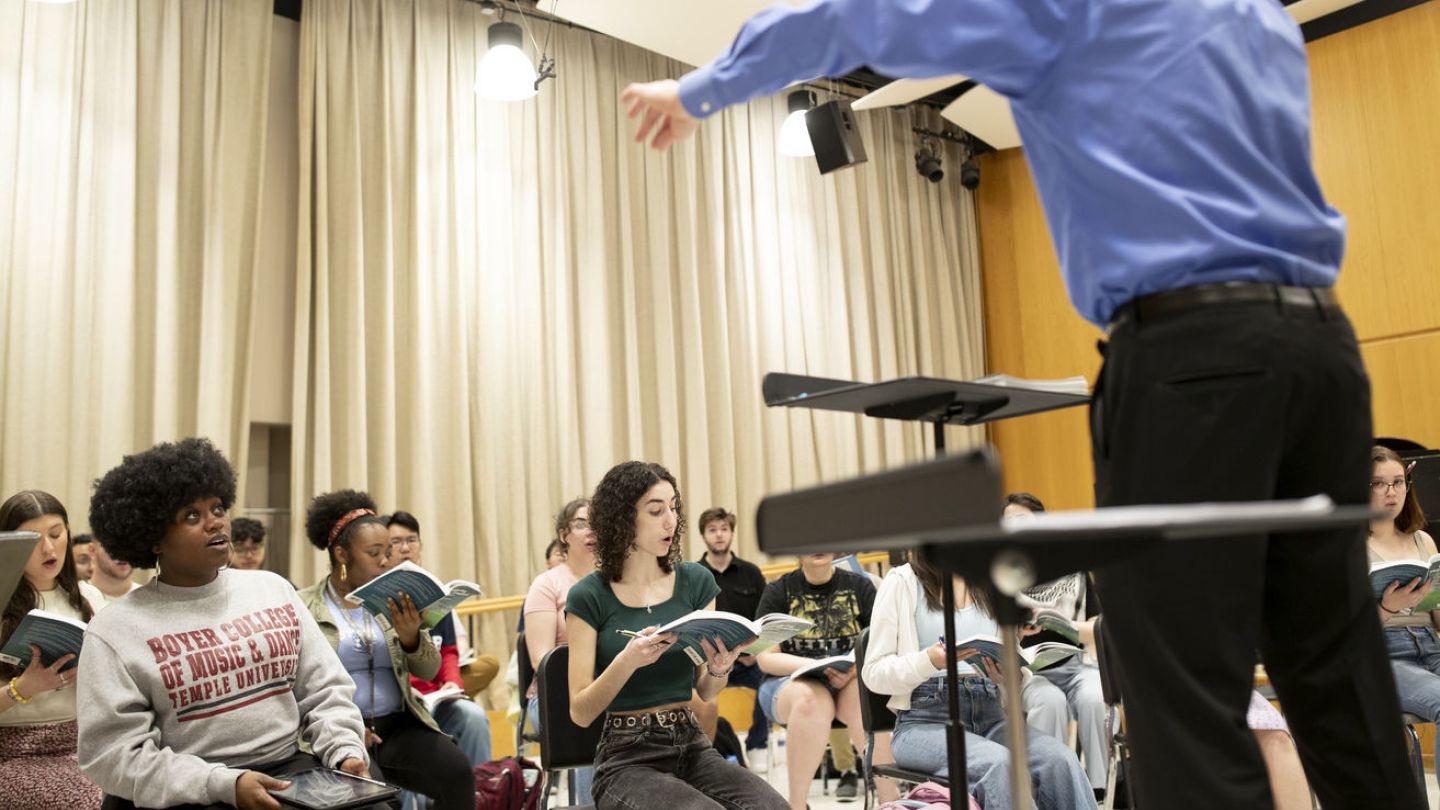 Photo of conductor leading choir in a rehearsal hall