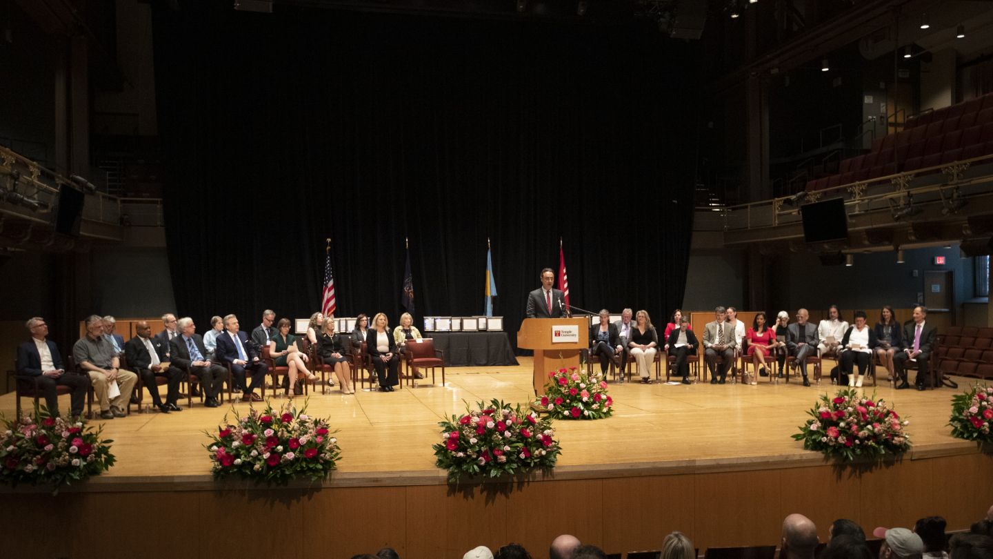 Photo of deans and awardees onstage with Provost Mandel speaking at podium