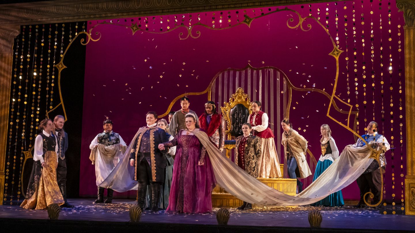 Large group of performers in costume onstage about to bow
