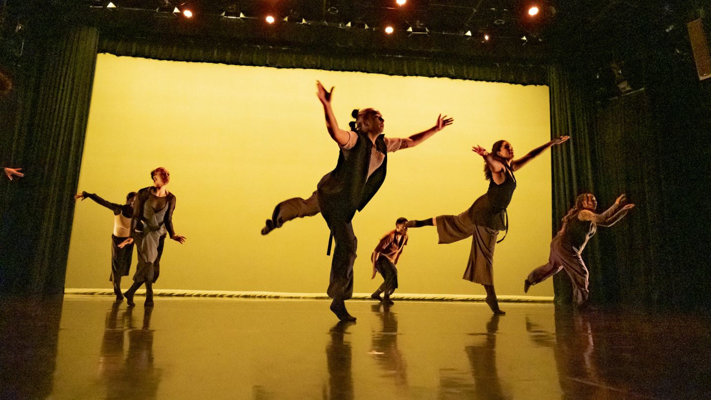 Photo of dancers performing against a yellow-lit backdrop